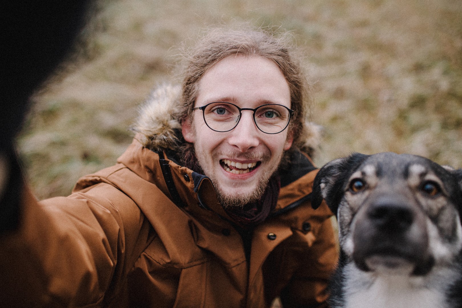 Fotol: Karl Erik Saks. Foto autor: Ken Mürk. PVC plaadile prinditud värvifoto. Formaat: A2 rõhtasendis (42x59,40cm). Foto kirjeldus: Portreefoto õues, pildistatud suunaga ülevalt alla. Rõõmsameelne noormees naeratab suurelt vaataja poole. Tal on tumesinised silmad ja ümara, musta peenikese raamiga prillid. Pruunid, kergelt lainelised pikad juuksed on üle pea kokku kammitud. Kõrge otsmik, terav nina. Lühike pruun habe ja vuntsid raamivad naeratavat suud. Karl Erikul on seljas helepruun paksem jope, mille krae ja kapuutsi sisemus on mustast kangast. Kapuutsi äär kirjukarvaline. Tema parem käsi on tõstetud vaataja suunas, mille otsas must, arusaamatu karvane kogu. Pildil paremal on pruunisilmne mustavalgekirju koer. Silmade ümber heledad laigud, koonu küljed ja kurgualune valge. Lühikesed, mustad, lontis kõrvad. Taustal hägustatud rohekas-pruunikas murupind.