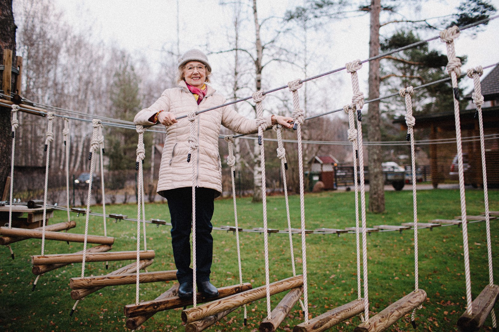 Fotol: Hele Lemetti. Foto autor: Ken Mürk. PVC plaadile prinditud värvifoto. Formaat: A2 rõhtasendis (42x59,40cm). Foto kirjeldus: Sügiseses pargis, puude vahele, maapinnast ligi 50 sentimeetri kõrgusele on trossidega kinnitatud kaks seiklusrada. Esiplaanil oleva raja peal seisab naerusuine, sale, väärikas eas, prillidega naine. Tema heledaid juukseid katab helehall ülesrullitud servaga kumer peakate, mille paremal pool on kaunistus. Helel on kaelas õhuke, kollase-punase-kirju sall. Seljas beežikas, tepitud, poolpikk jope. Jalas mustad pikad püksid ja mustad saapad. Ta hoiab mõlema käega kinni seiklusraja trossidest ja seisab jalad koos, ühe, umbes 15 sentimeetrise läbimõõduga ümara prussi peal. Ümaratest prussidest tehtud ühe meetri laiust siksakilist rada hoiab ühenduses köis. Rada algab foto vasakust servas puu külge kinnitatult ja kulgeb kuni foto parempoolse servani. Iga prussi serva on kinnitatud vertikaalne köis, mis kinnitub spetsiaalse sõlme abil horisontaalsele trossile. Taamal, paremal on üks mänd ja hoone, mille varikatuse alla on pargitud hall auto. Pildil vasakul näha üks okaspuu ja raagus kasesalu. Roheline muru on täis kollakas- tumepruune lehti.